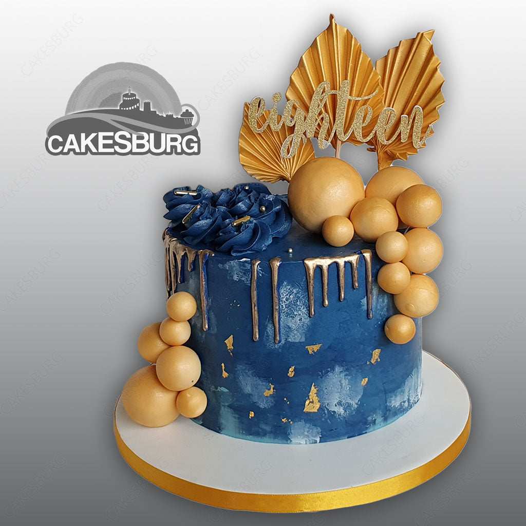 Moist Vanilla cake layers sandwiched with simple buttercream, covered with dark  blue shaded buttercream and decorated with silky smooth white chocolate  ganache with flowers, cookies and chocolate. It's made under the theme
